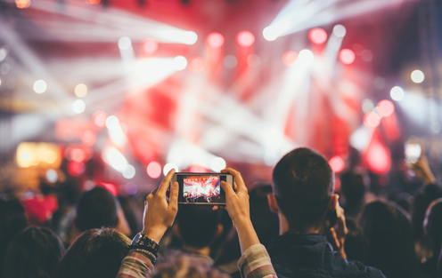 person holds phone above concert crowd to capture the moment